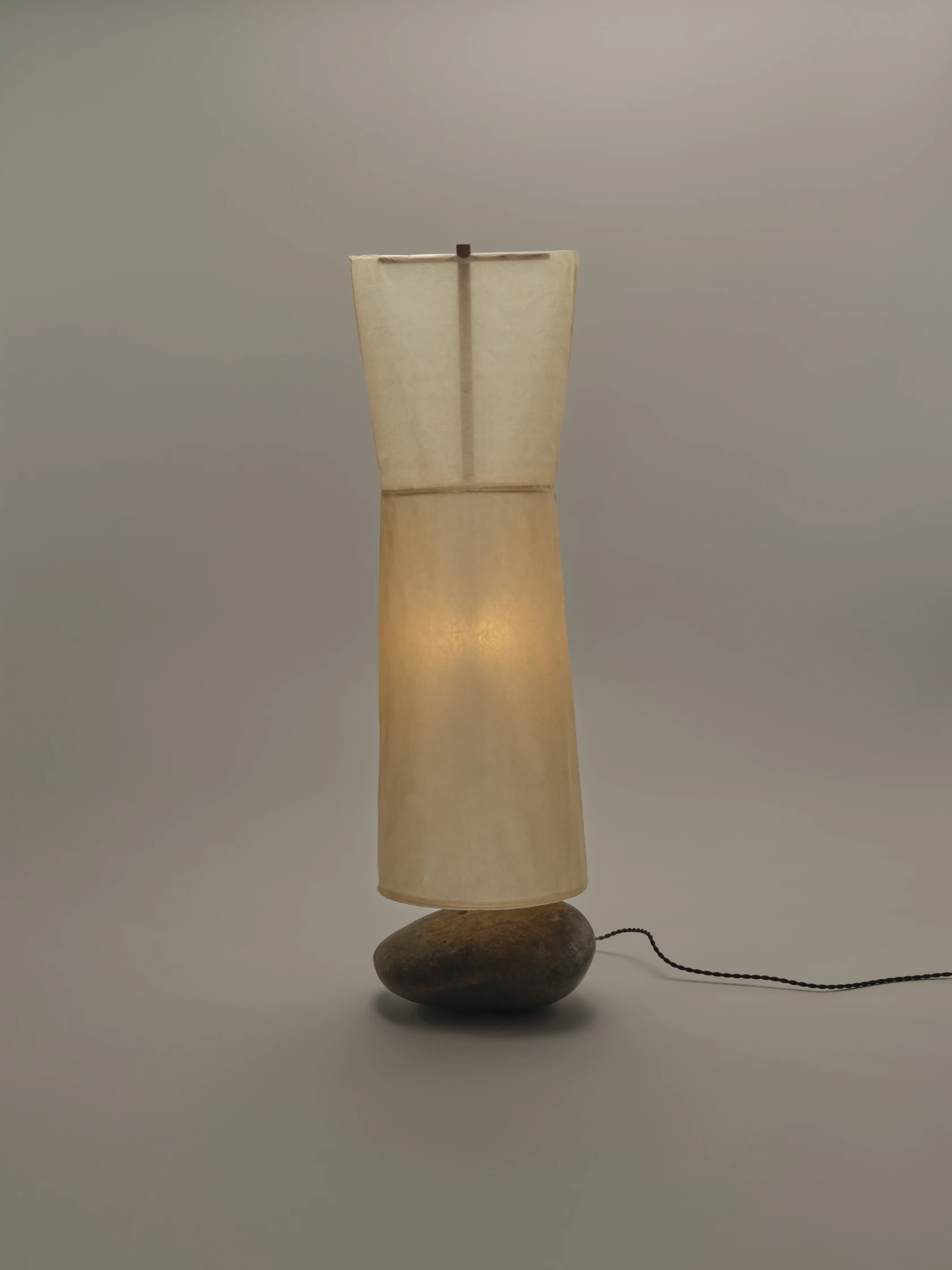 A floor lamp with a translucent paper or fabric shade resting on a solid river stone base.