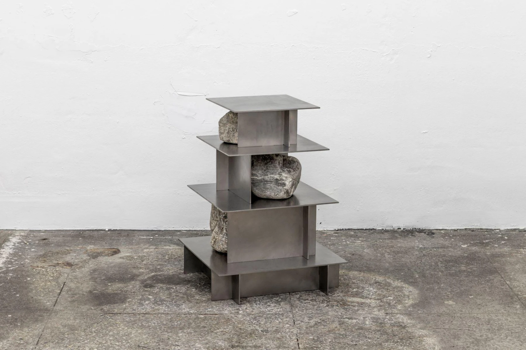 A shelving unit constructed from folded sheet metal and stacked natural stones, forming a miniature pagoda-like structure.