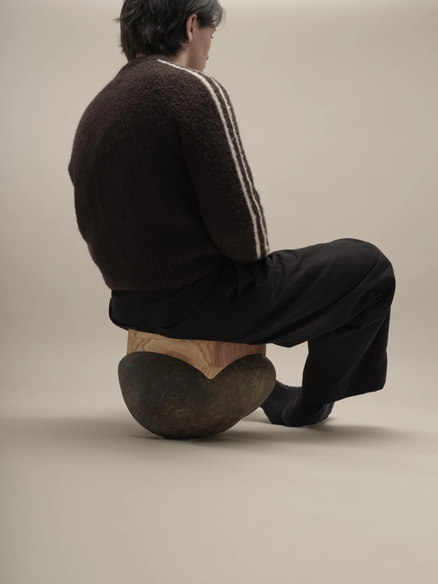 A seating object combining a natural river stone and a fitted wooden seat and a person sitting on it.